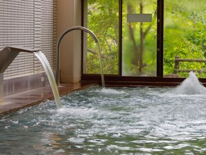 A hot tub with a metal faucet and a view of greenery through a glass door.