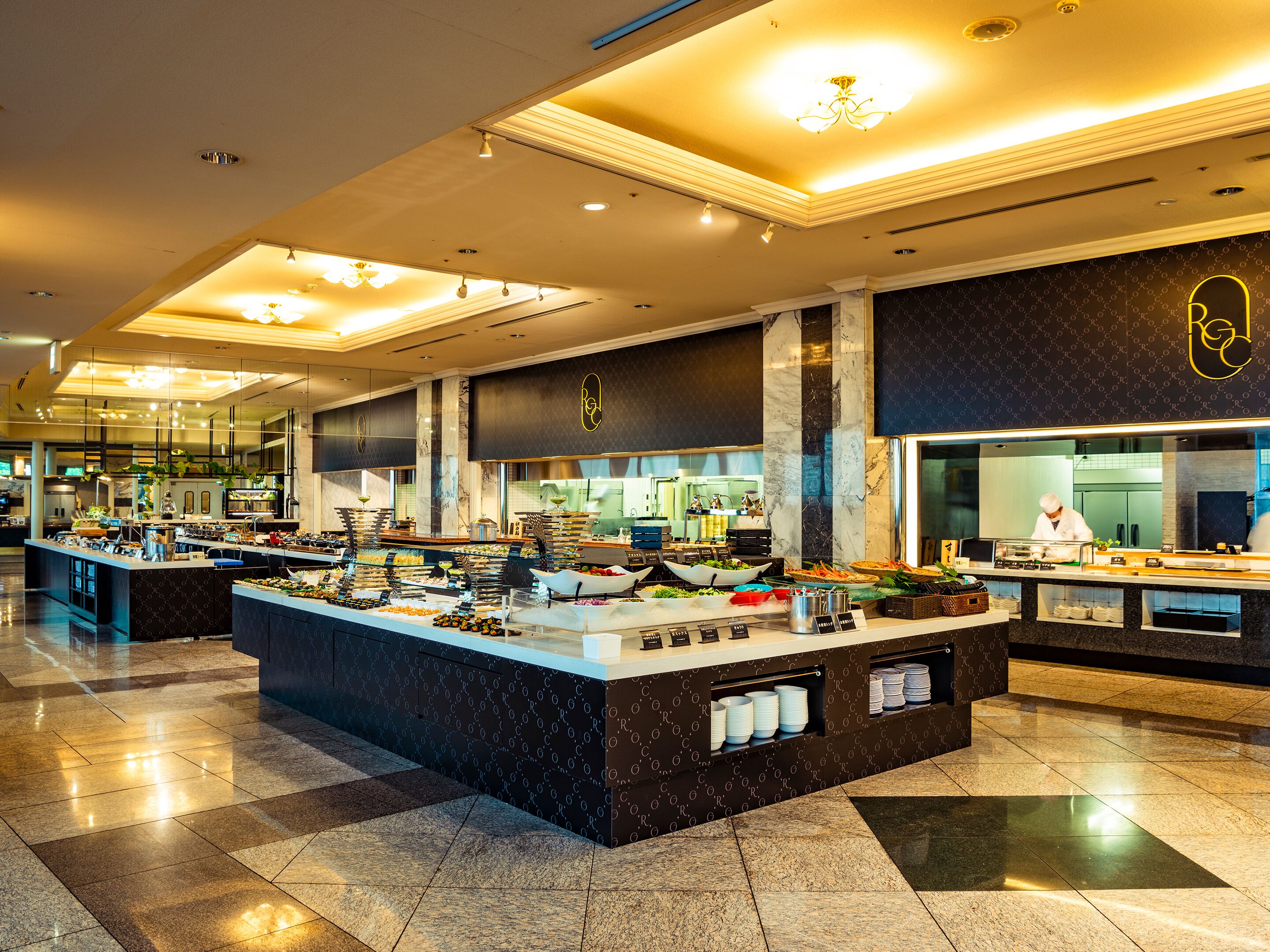 A buffet setup with various food stations, a chef preparing food, and a modern interior design.