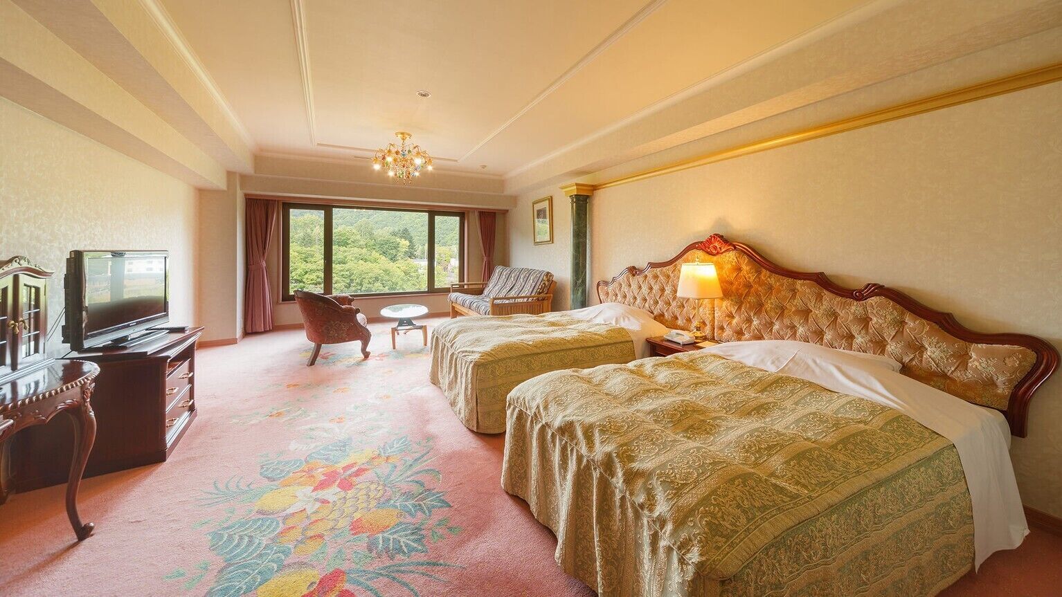 A hotel room with two beds, a television, a desk, and a view of greenery.