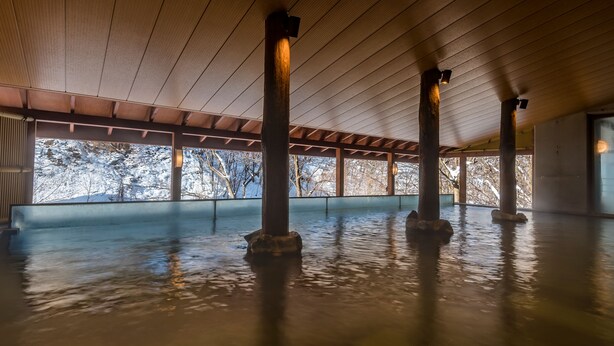 A spacious indoor area with a high ceiling and wooden beams, featuring large windows that offer a view of snow-covered trees. - Jozankei View Hotel (Sapporo)