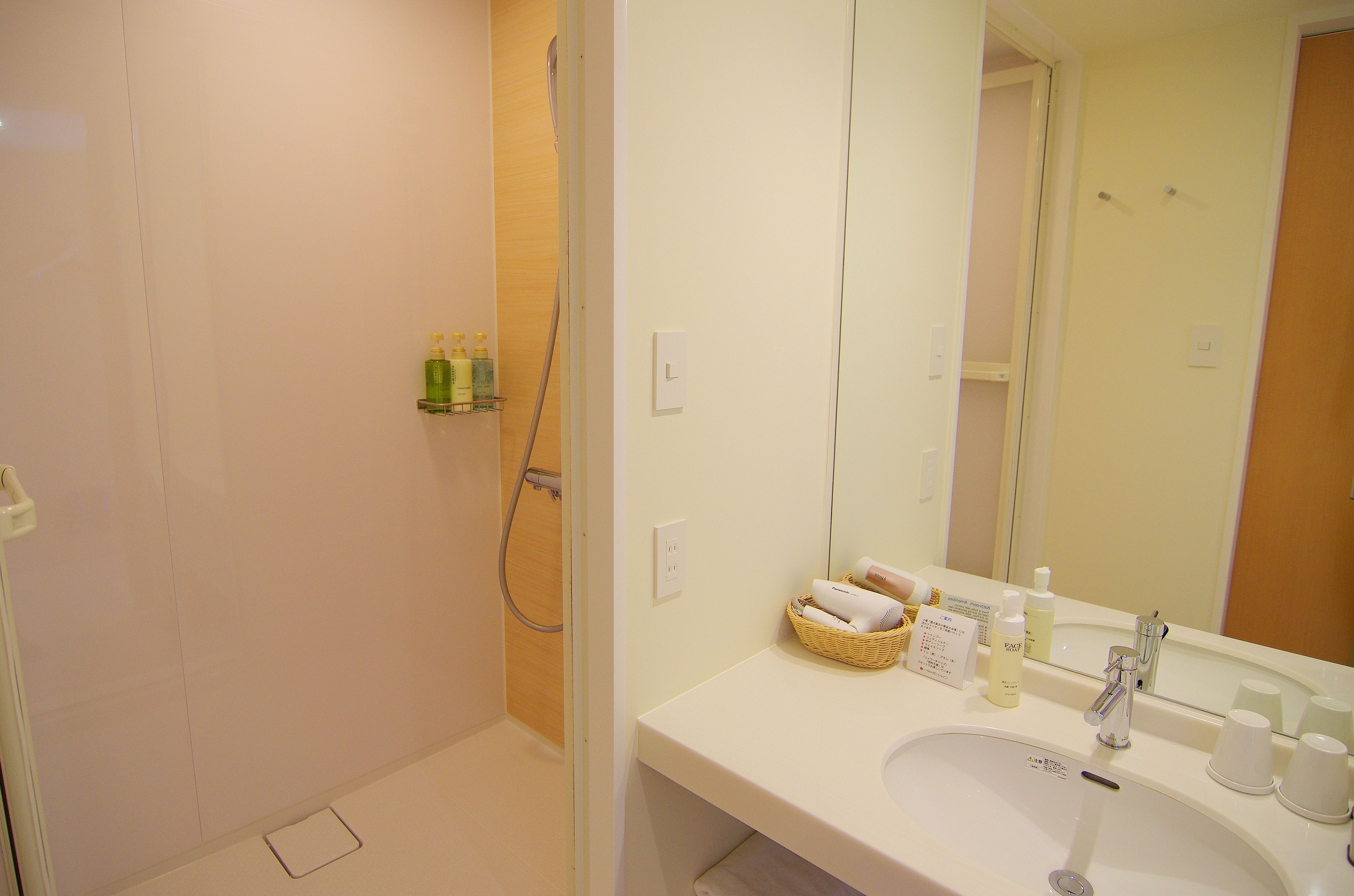 A bathroom with a shower, a sink with toiletries, and a mirror.