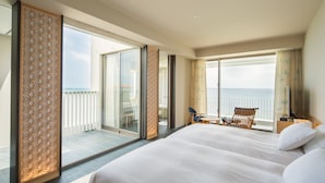 Ein Hotelzimmer mit einem großen Bett, einem Balkon mit Meerblick und einer Sitzecke mit Tisch und Stühlen.