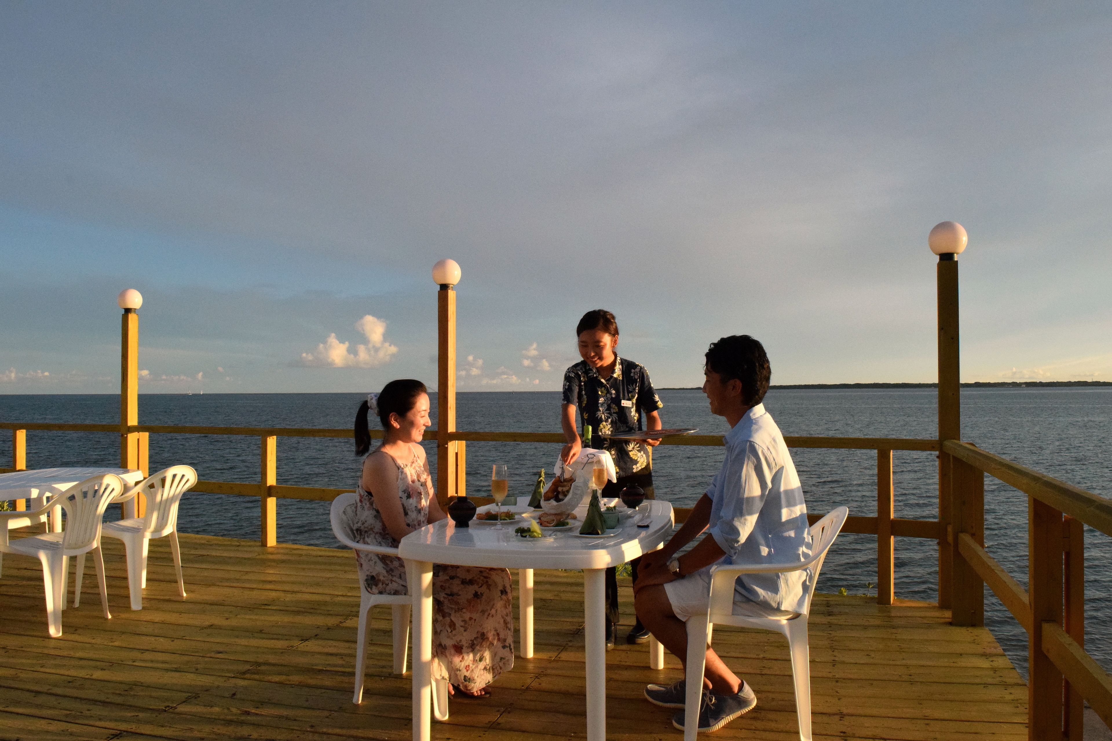 Une terrasse en bois avec des chaises en plastique blanches et une table dressée pour un repas.