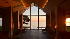 Ein geräumiges Zimmer mit großen Fenstern und Blick auf das Meer bei Sonnenuntergang.