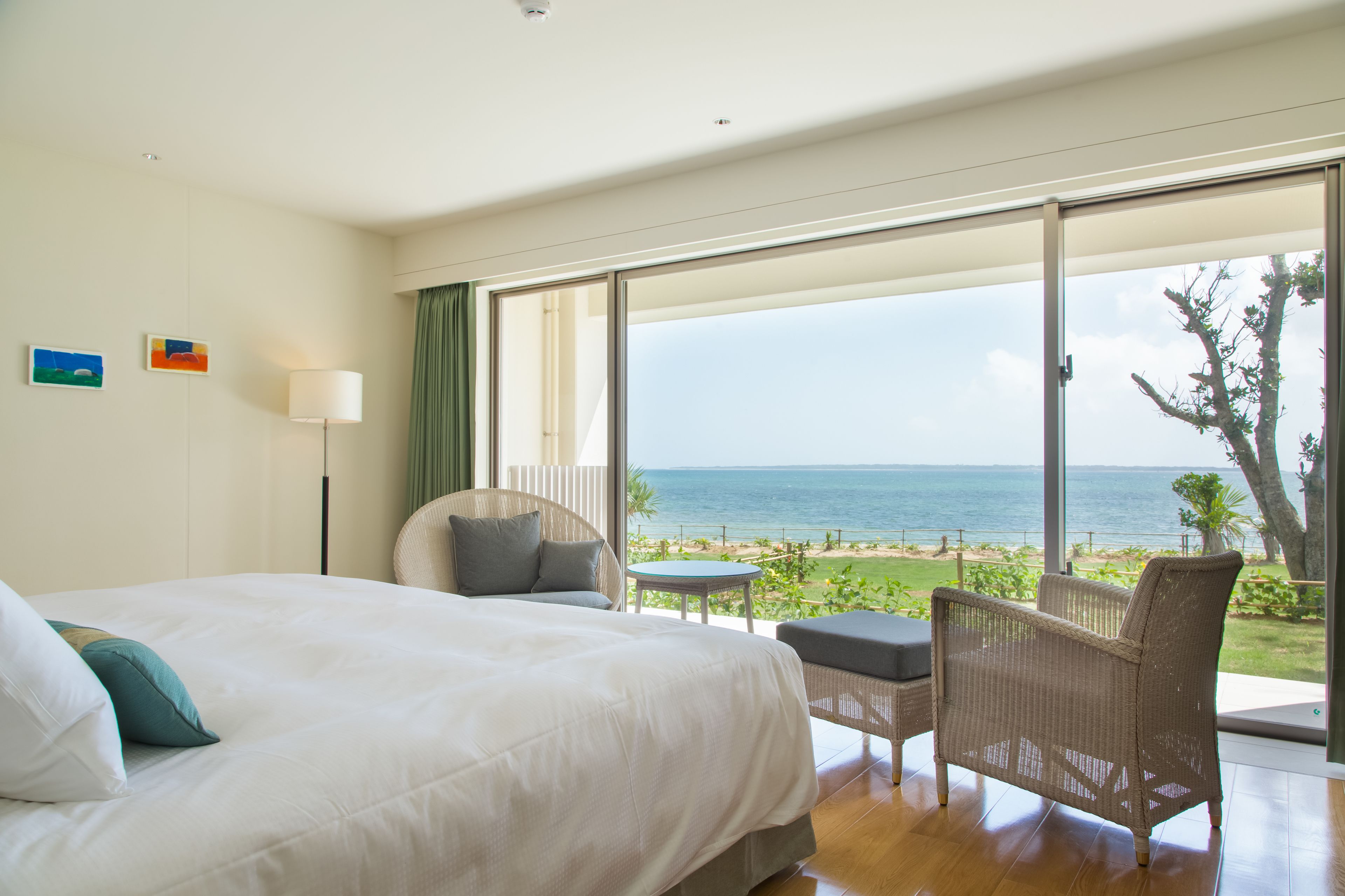 A bedroom with a large bed, a chair, a small table, and a view of the ocean.