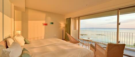 Een hotelkamer met een groot bed, een stoel en een balkon met uitzicht op zee.