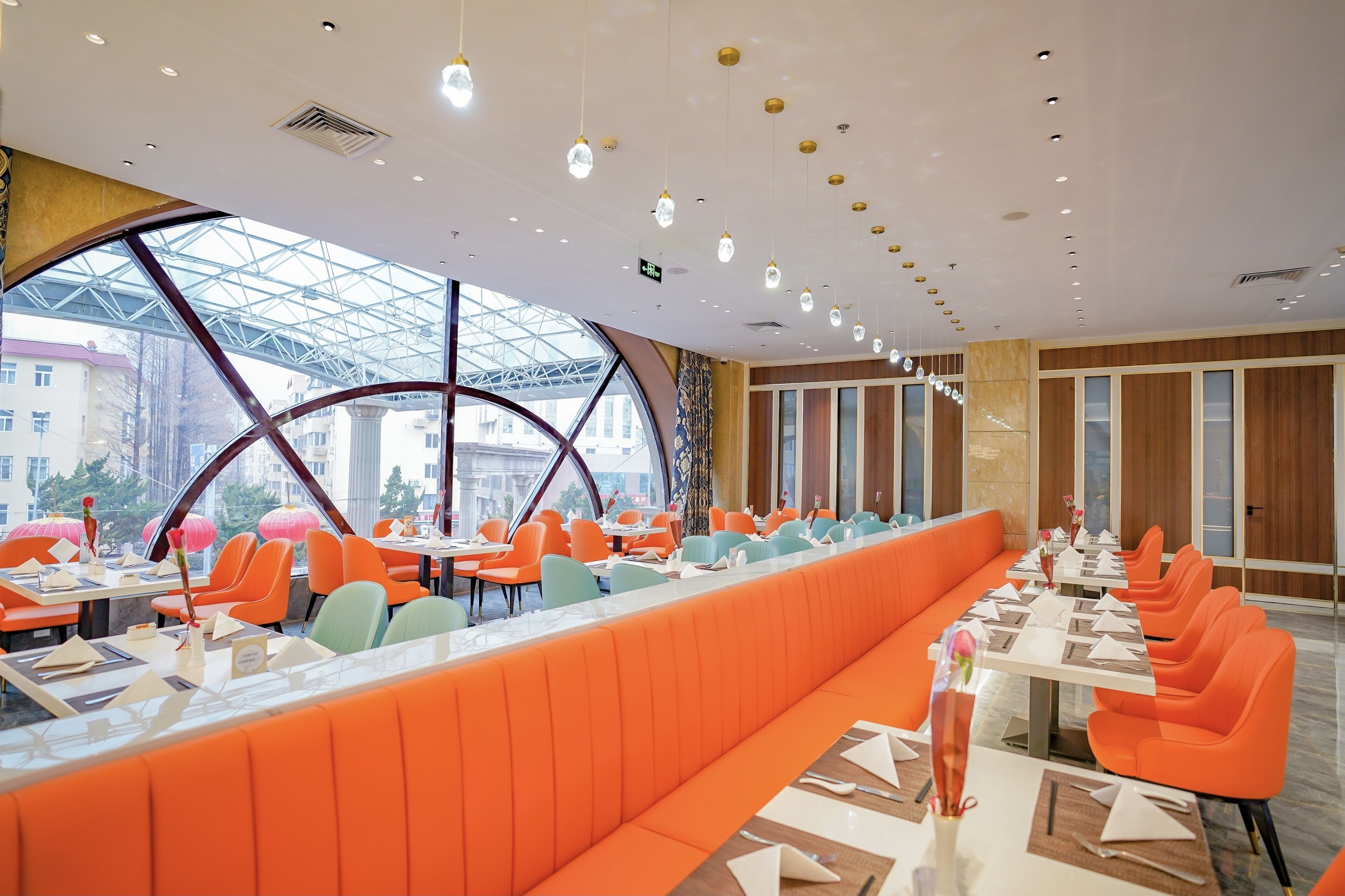 Un restaurant moderne avec des sièges orange, de grandes fenêtres et un plafond en verre.