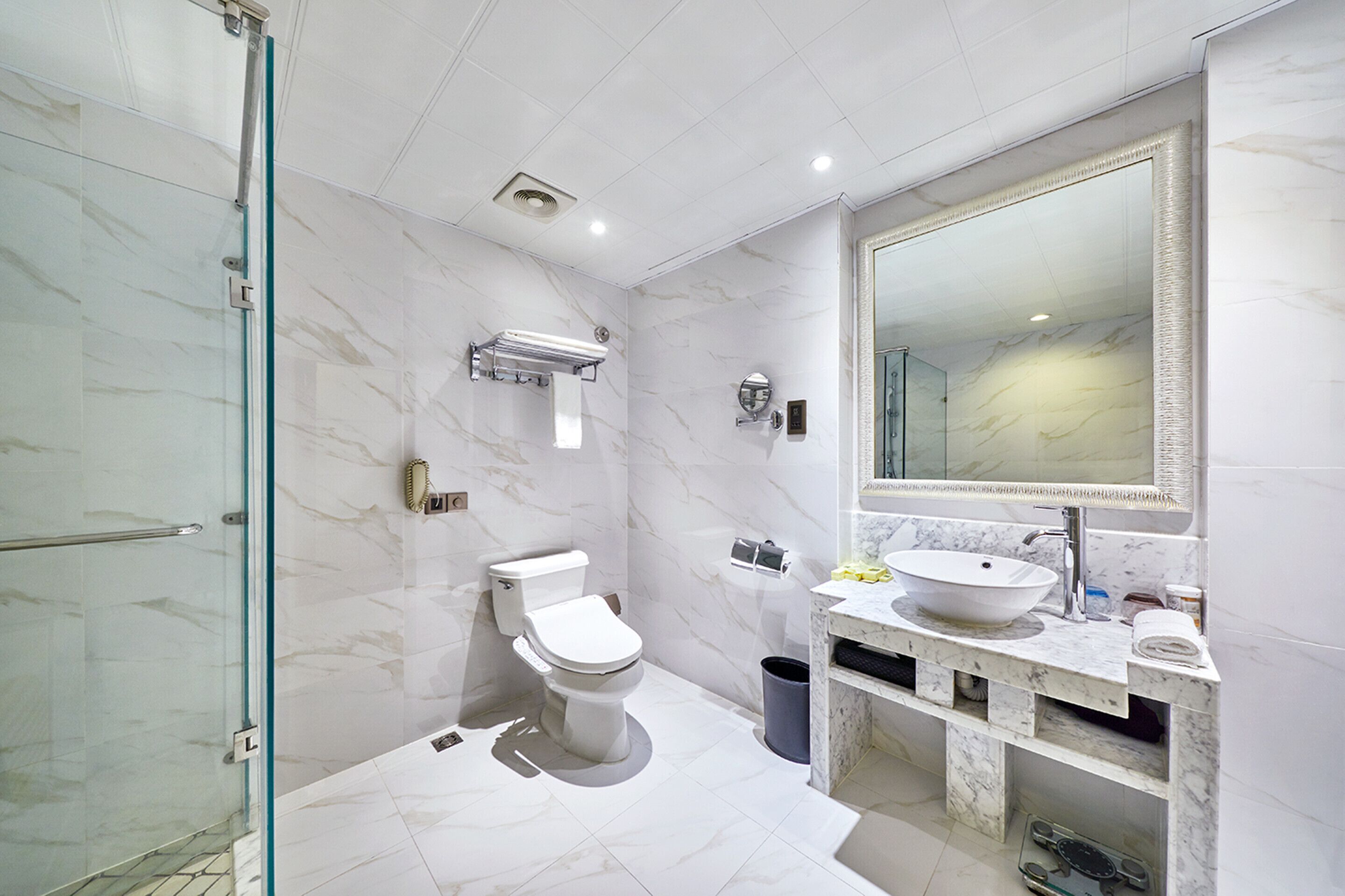 Une salle de bain moderne avec une douche à parois de verre, des toilettes, un lavabo avec un grand miroir et un revêtement de sol en marbre.