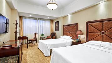 A hotel room with two beds, a desk, a chair, a TV, and a lamp.