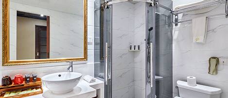 Un baño moderno con lavamanos blanco, un espejo grande, una ducha con mampara de vidrio y un inodoro.