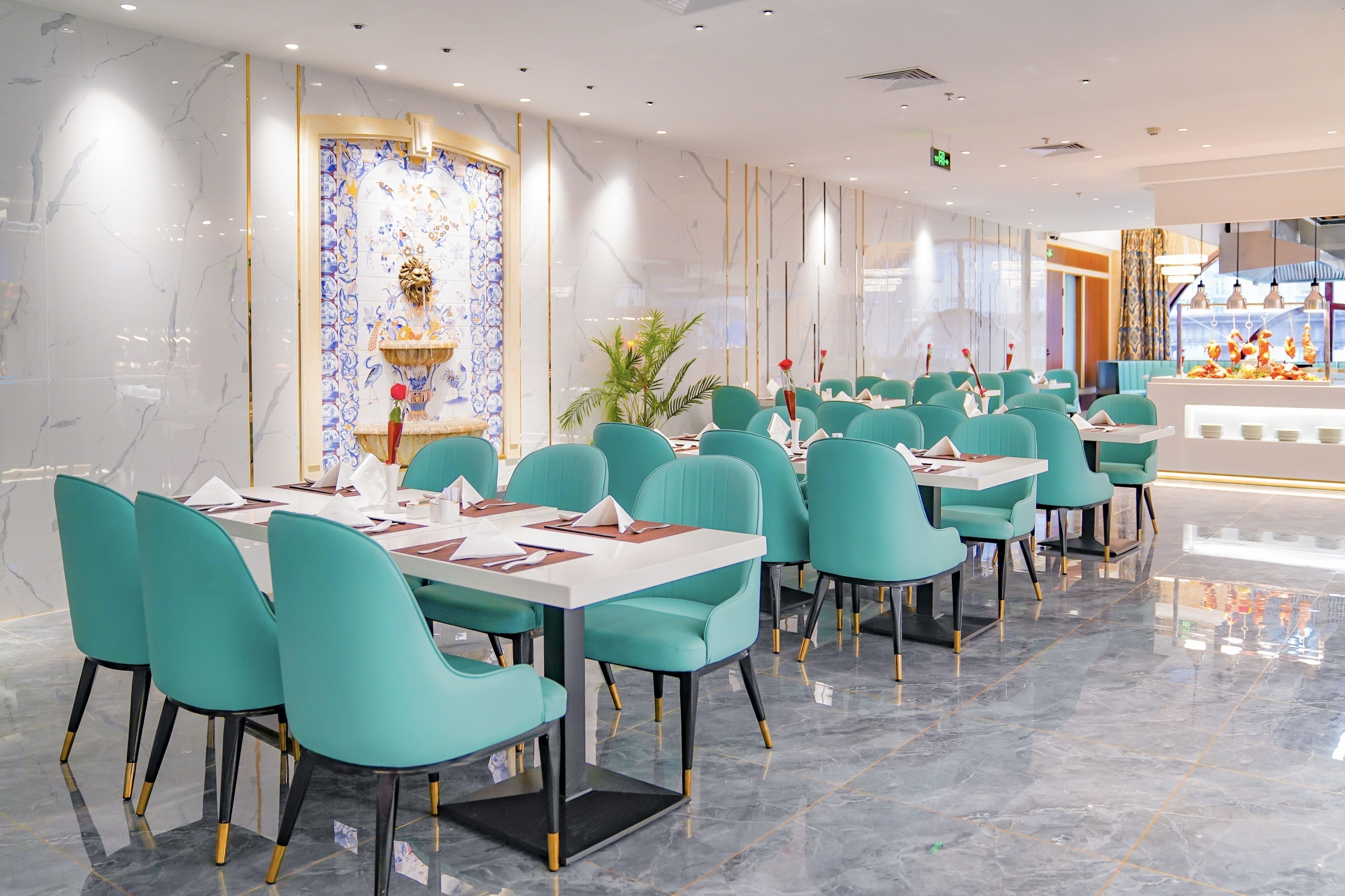 Een modern restaurant met teal stoelen en witte tafels, marmeren wanden en een decoratief paneel.