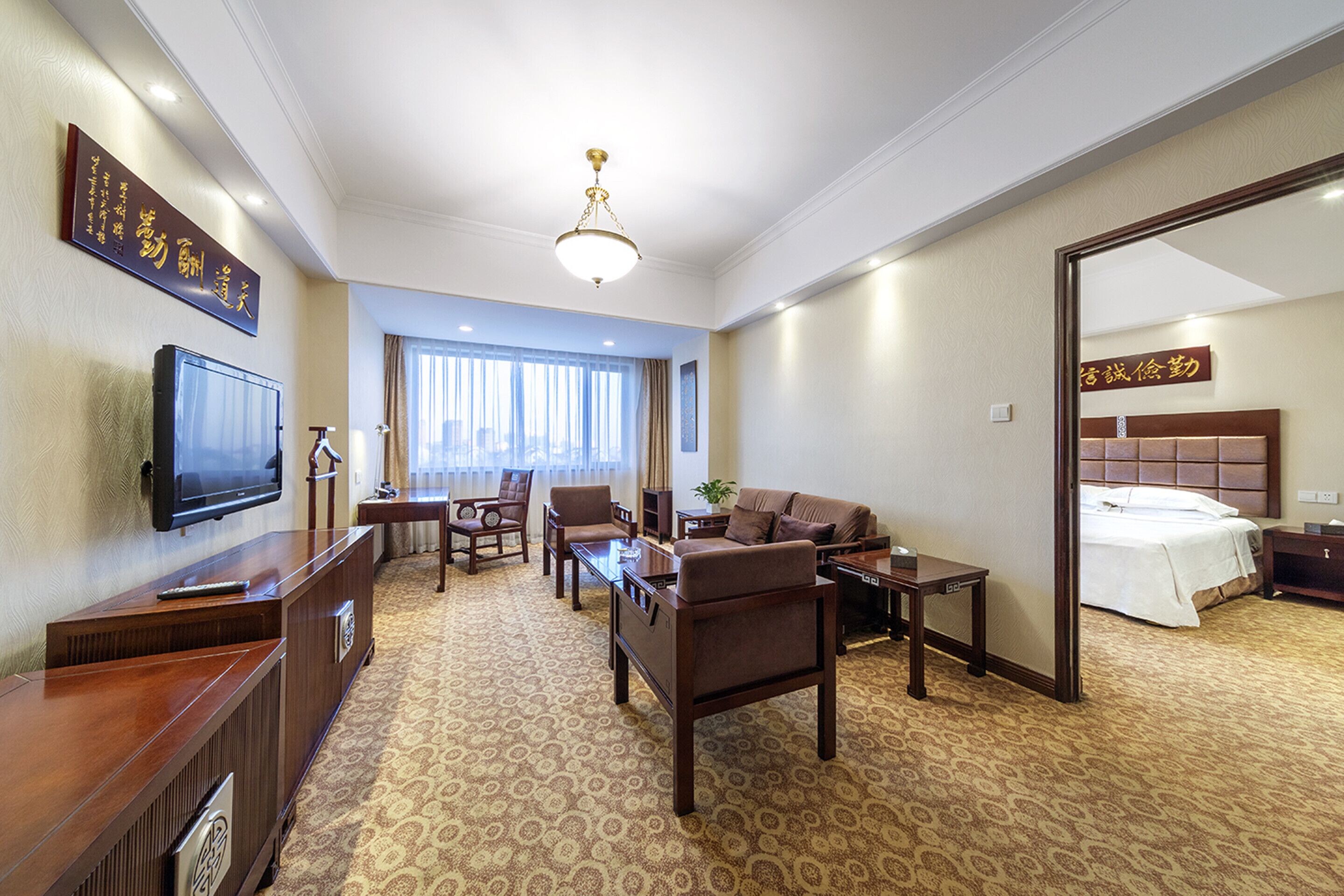 A hotel room with a television, sofa, armchair, coffee table, and a bed with a headboard.