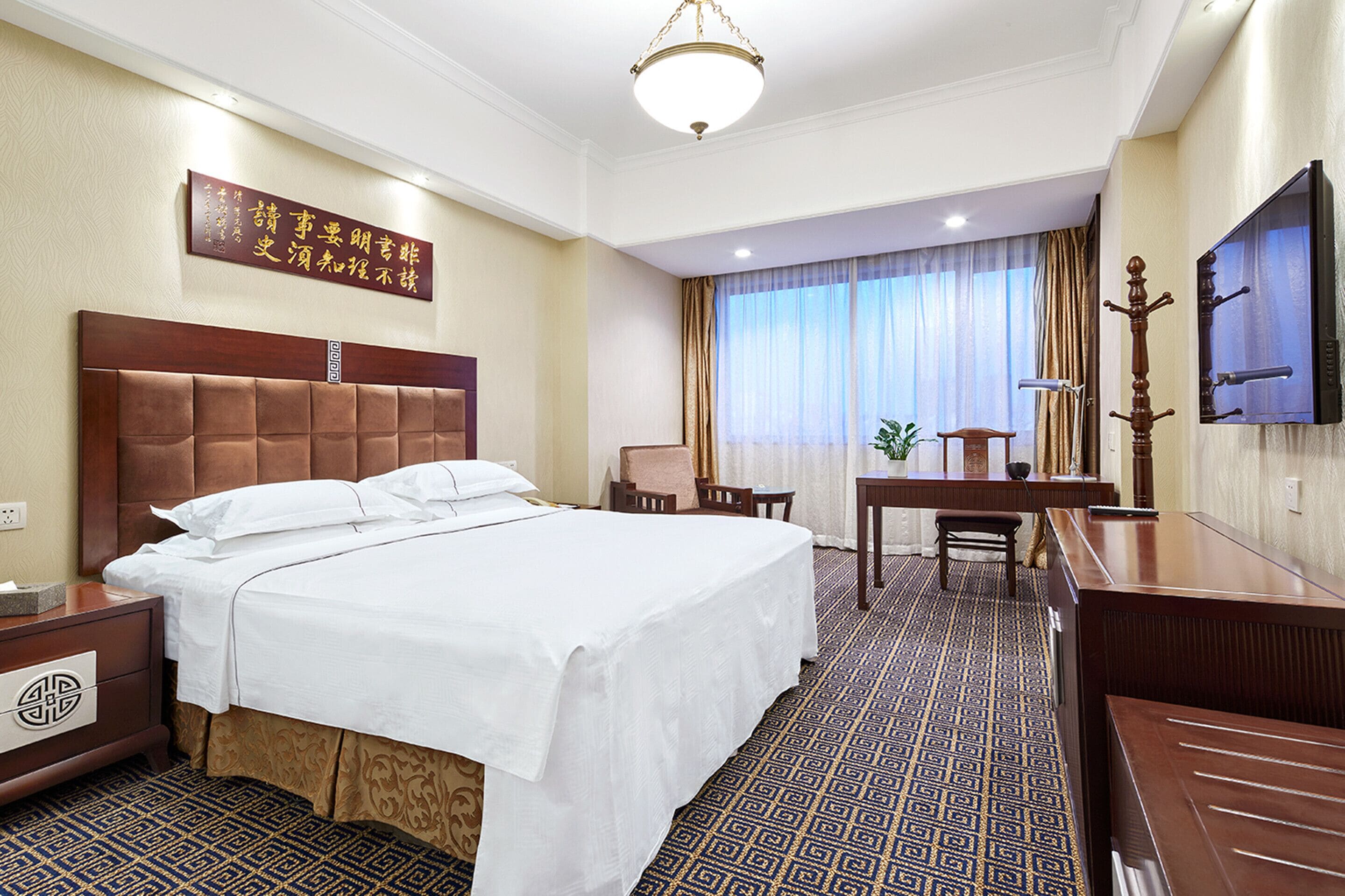 A hotel room with a large bed, a desk, a chair, a television, and a decorative wall piece.