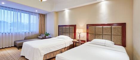 A hotel room with two beds, a sofa, a small table with a lamp, and a large window with curtains.
