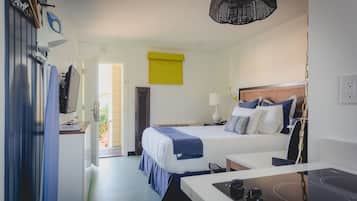 A hotel room with a bed, bedside table, lamp, and a kitchenette area.