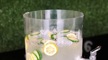 A clear glass with ice and lemon slices, placed on a reflective surface with a faucet.
