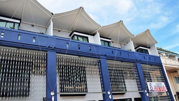 Un edificio con fachada azul, grandes ventanales con persianas verticales y un cartel que indica que el establecimiento est á ahora abierto.