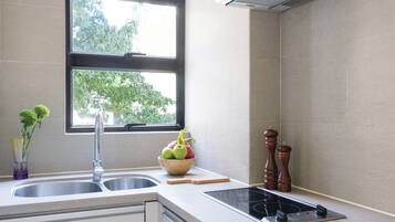 A kitchen with a double sink, a window, a bowl of fruit, a cutting board, and a stove.