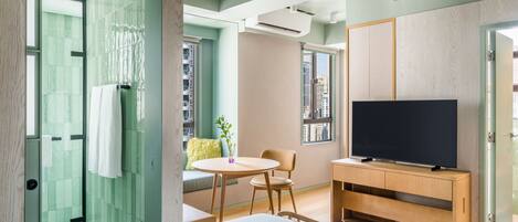Habitación de hotel moderna con cama, televisión, un pequeño comedor y vistas a la ciudad.