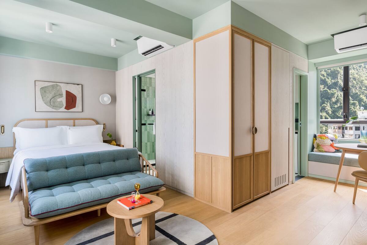 A modern bedroom with a bed, a sofa, a wardrobe, and a window with a view of buildings.