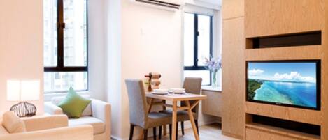 A modern living room with a flat-screen TV, a dining area, and large windows.