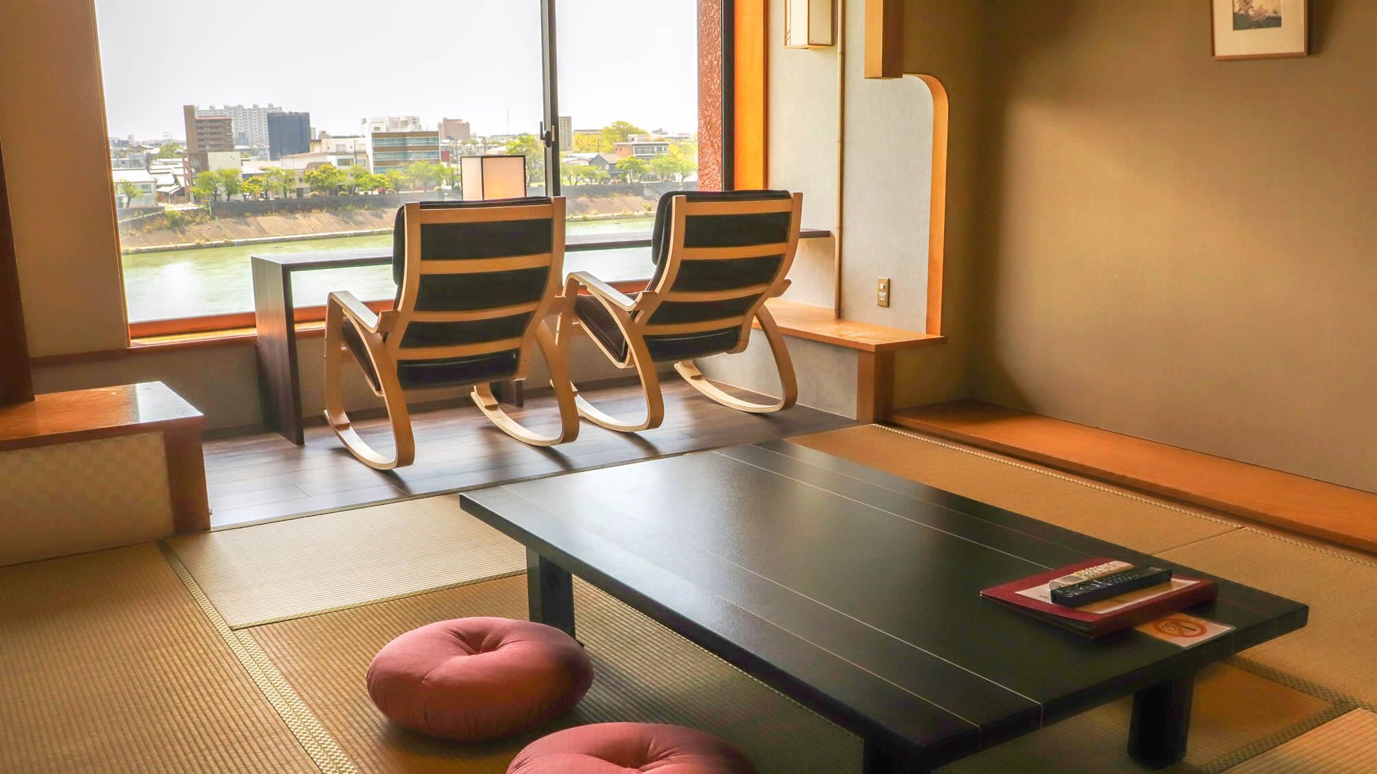 A room with two rocking chairs, a low table, and a view of a cityscape through a large window.