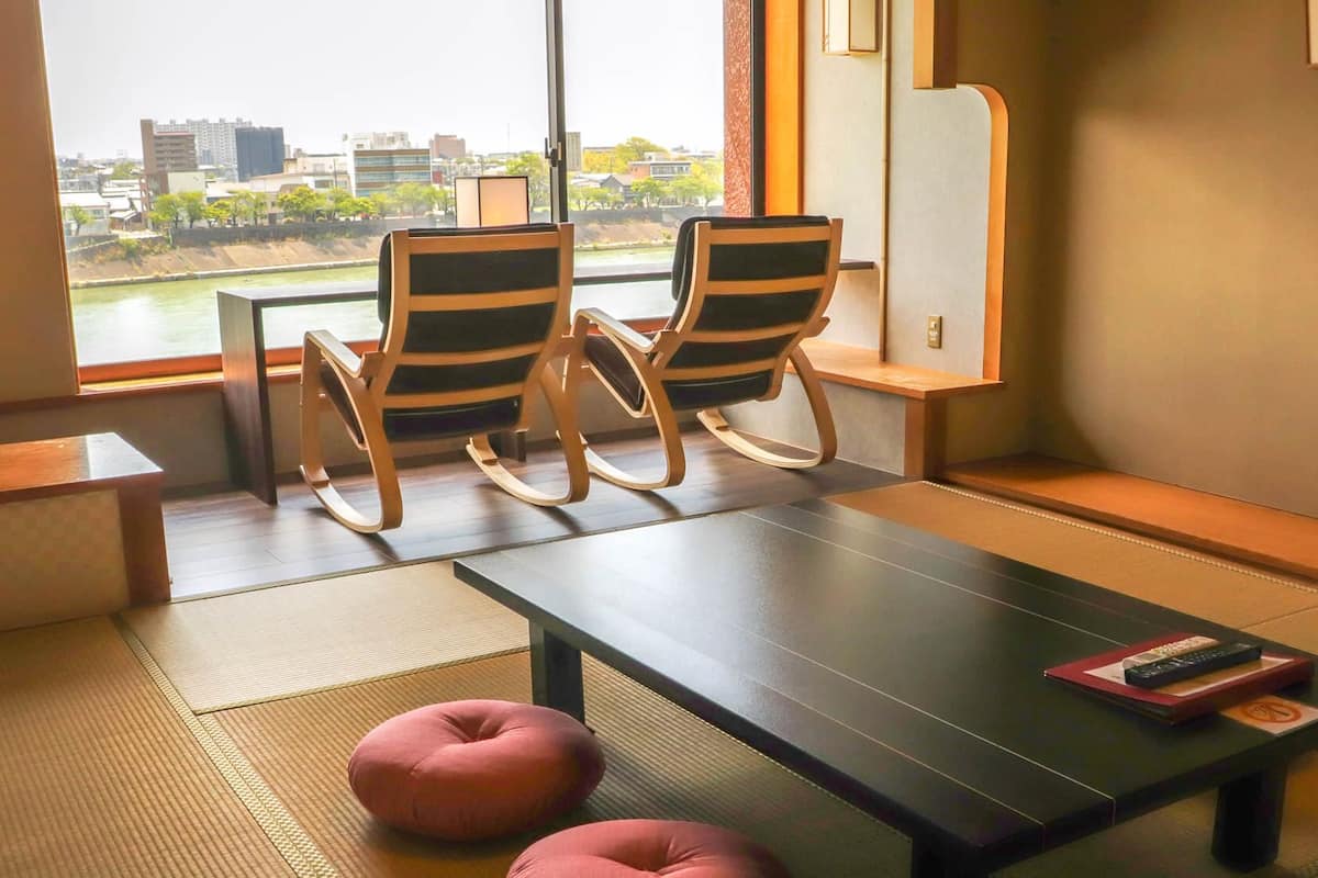 Una habitación con dos mecedoras, una mesita baja y vistas a un paisaje urbano a través de un ventanal grande.