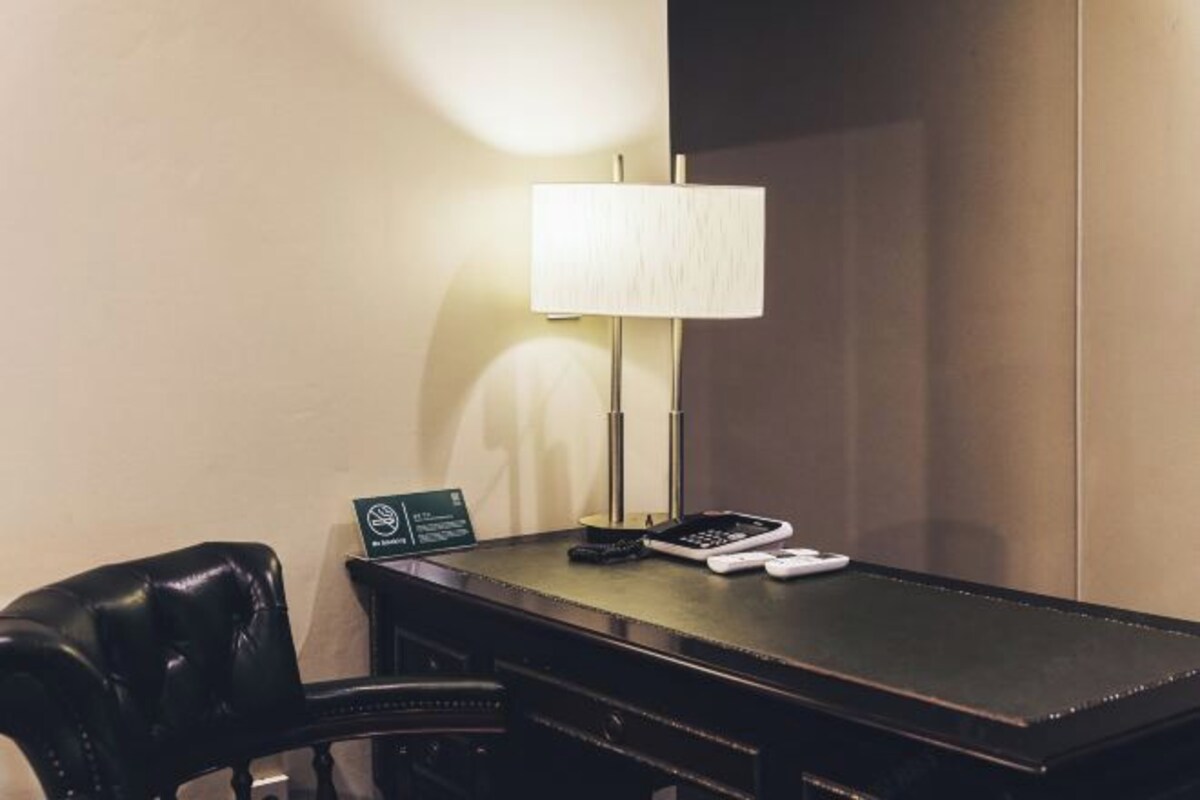 Et hotelværelse med skrivebord, lampe, stol og skilt.