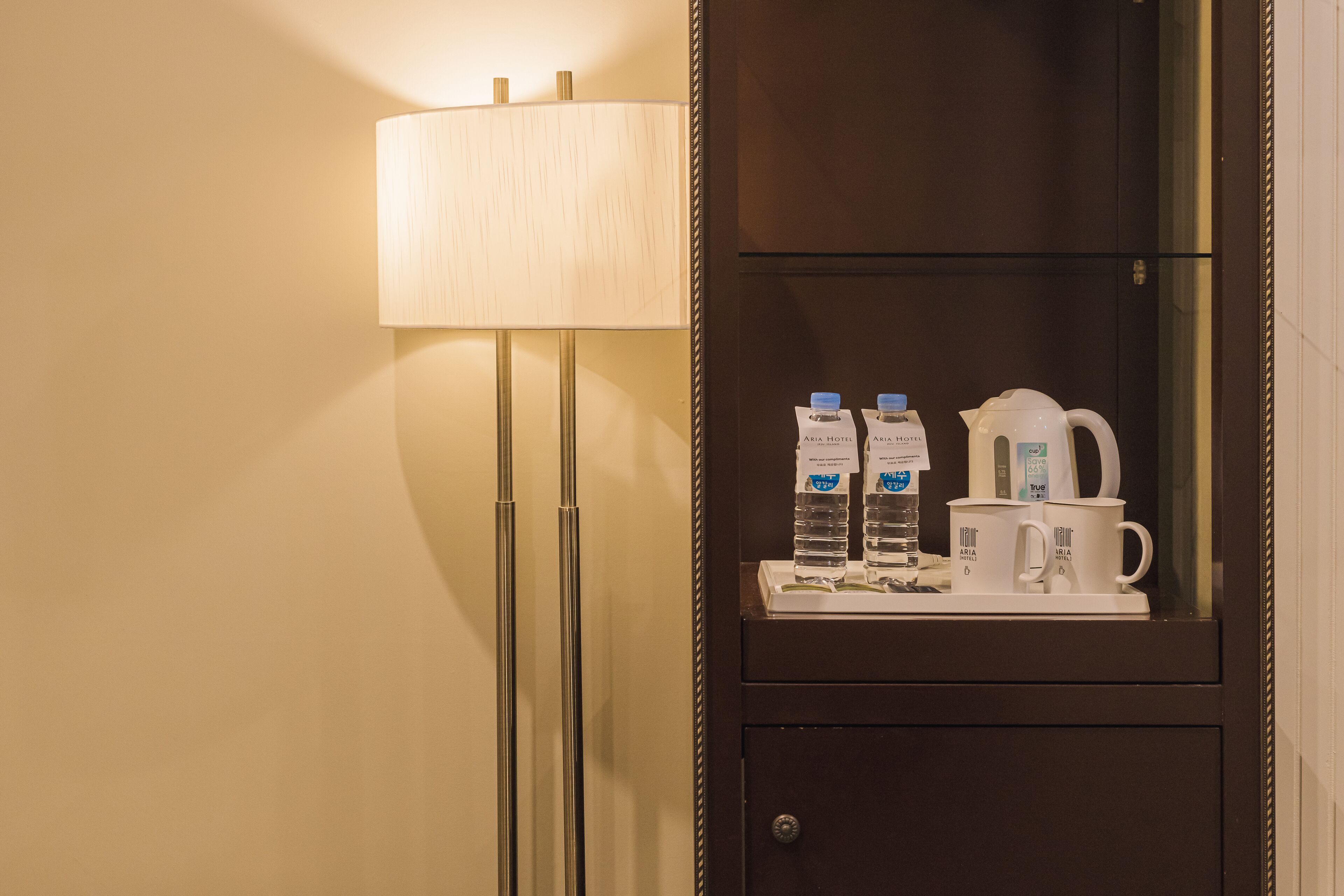 Habitación de hotel con mesita de noche que presenta una cafetera, dos botellas de agua y dos tazas con el logotipo del hotel.