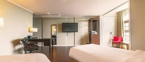 Habitación de hotel con dos camas, un escritorio con silla, televisor y armario.