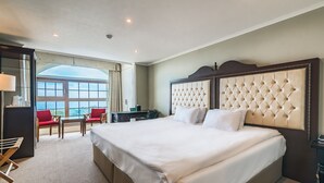 A spacious hotel room with a large bed, a desk, and a chair. There is a window with a view of the sky. - Aria Hotel Jeju (Seogwipo)