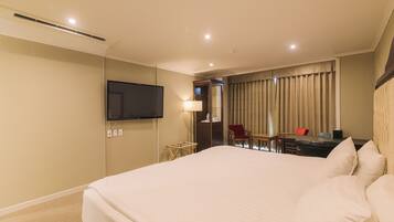A hotel room with a large bed, a desk with a chair, a television mounted on the wall, and a window with curtains.