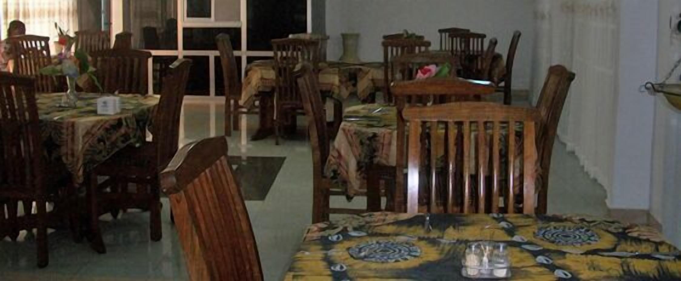 A dining area with wooden tables and chairs, some covered with tablecloths, and a vase with flowers on one table.