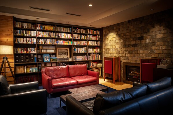 Una sala de estar acogedora con un sofá de cuero rojo, un sofá de cuero negro y una chimenea. Un estante grande lleno de libros se encuentra al fondo.