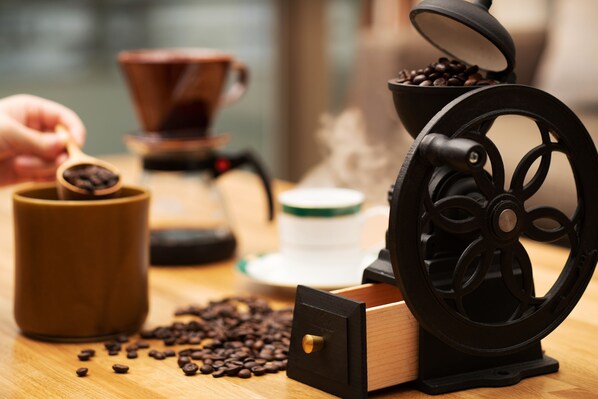 Un molinillo de café, una taza de café y granos de café esparcidos sobre una superficie de madera.