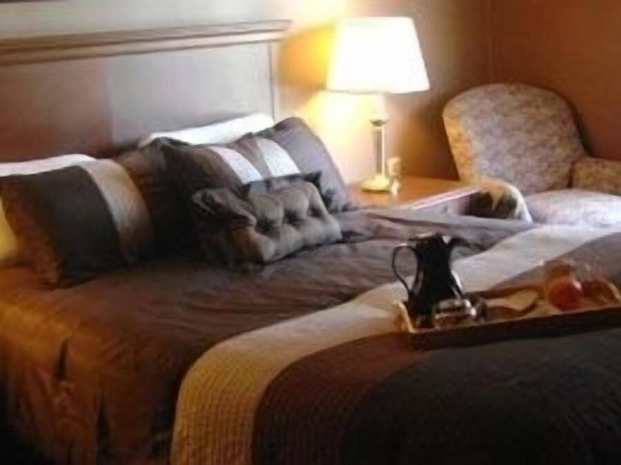 Una habitación de hotel con una cama grande, dos lámparas de noche, una silla y una bandeja con una taza y un platillo.
