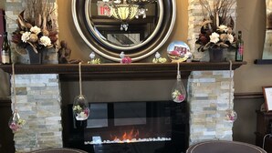 A fireplace with a stone mantle, two upholstered chairs, and a chandelier.