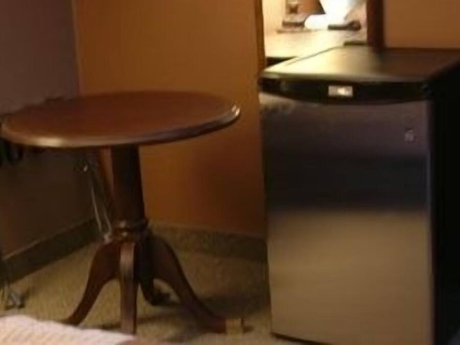 A compact hotel room with a small wooden table and a compact refrigerator.