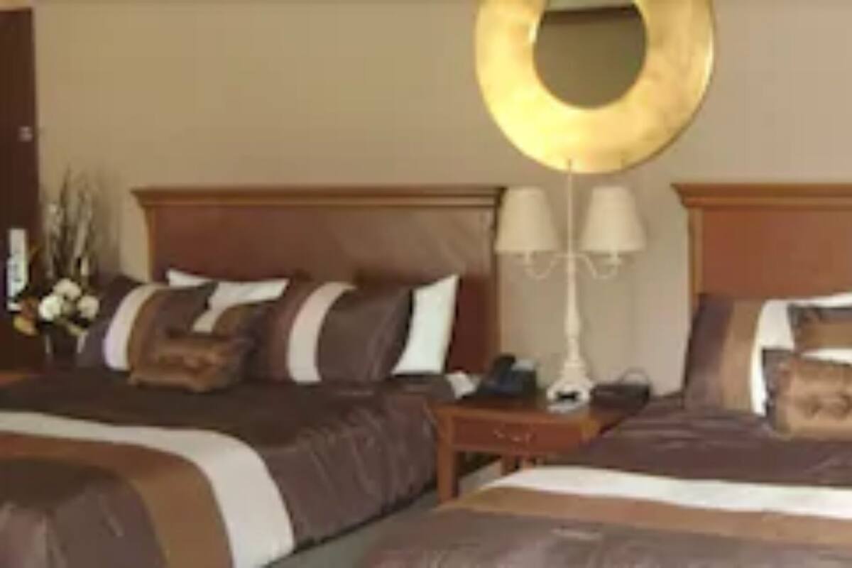 A hotel room with two beds, each with a wooden headboard, a bedside table, and a lamp.