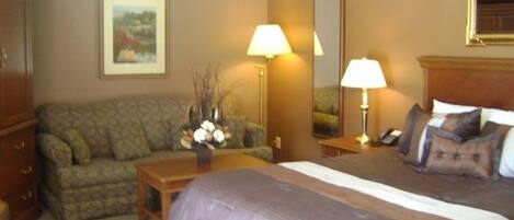 A hotel room with a bed, a sofa, a desk, and a lamp.