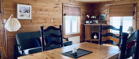 Interior de una cabaña de madera con una mesa de comedor, sillas, un sofá y un armario.