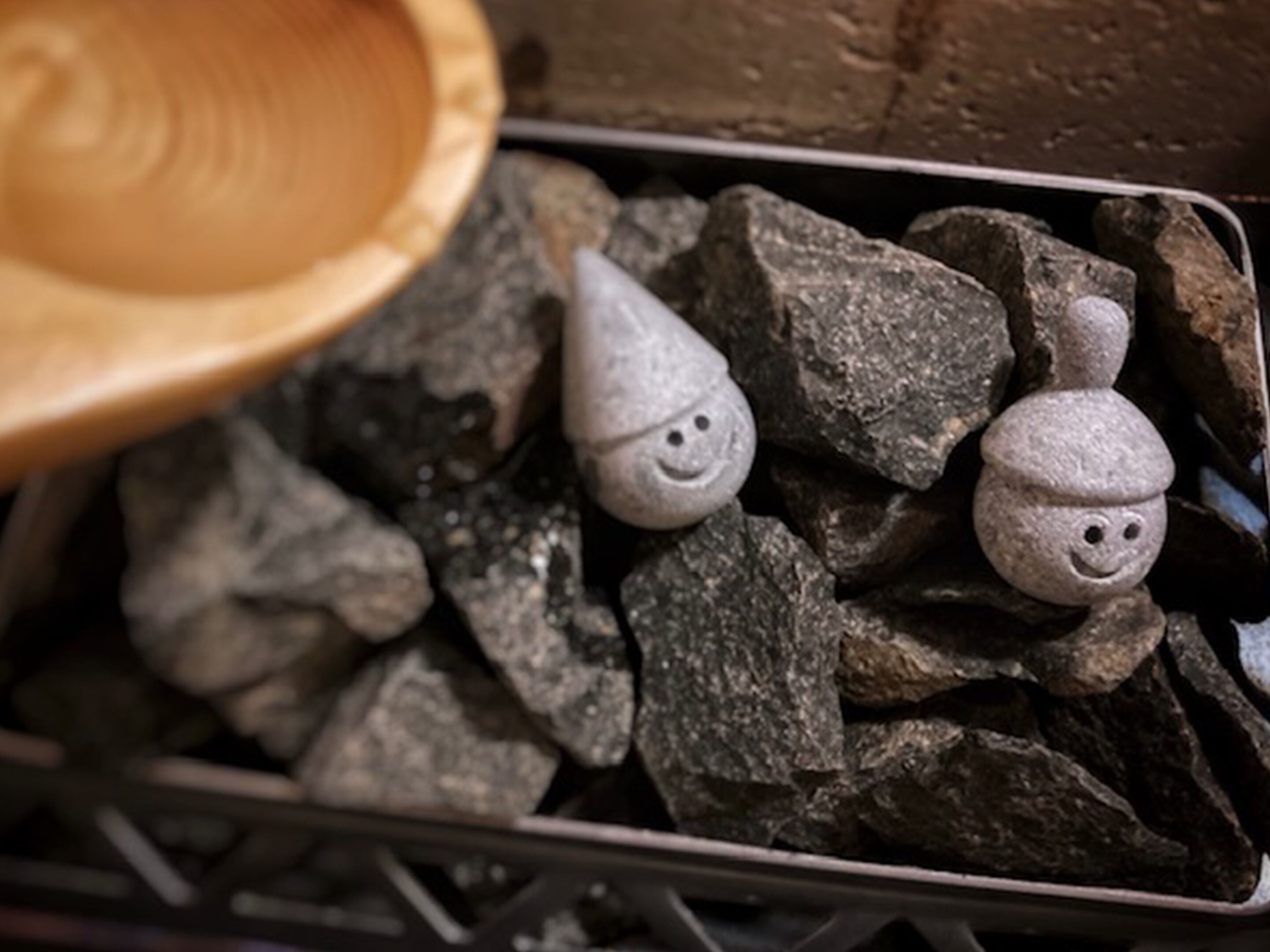 A metal basket filled with rocks and two stone figures with faces.
