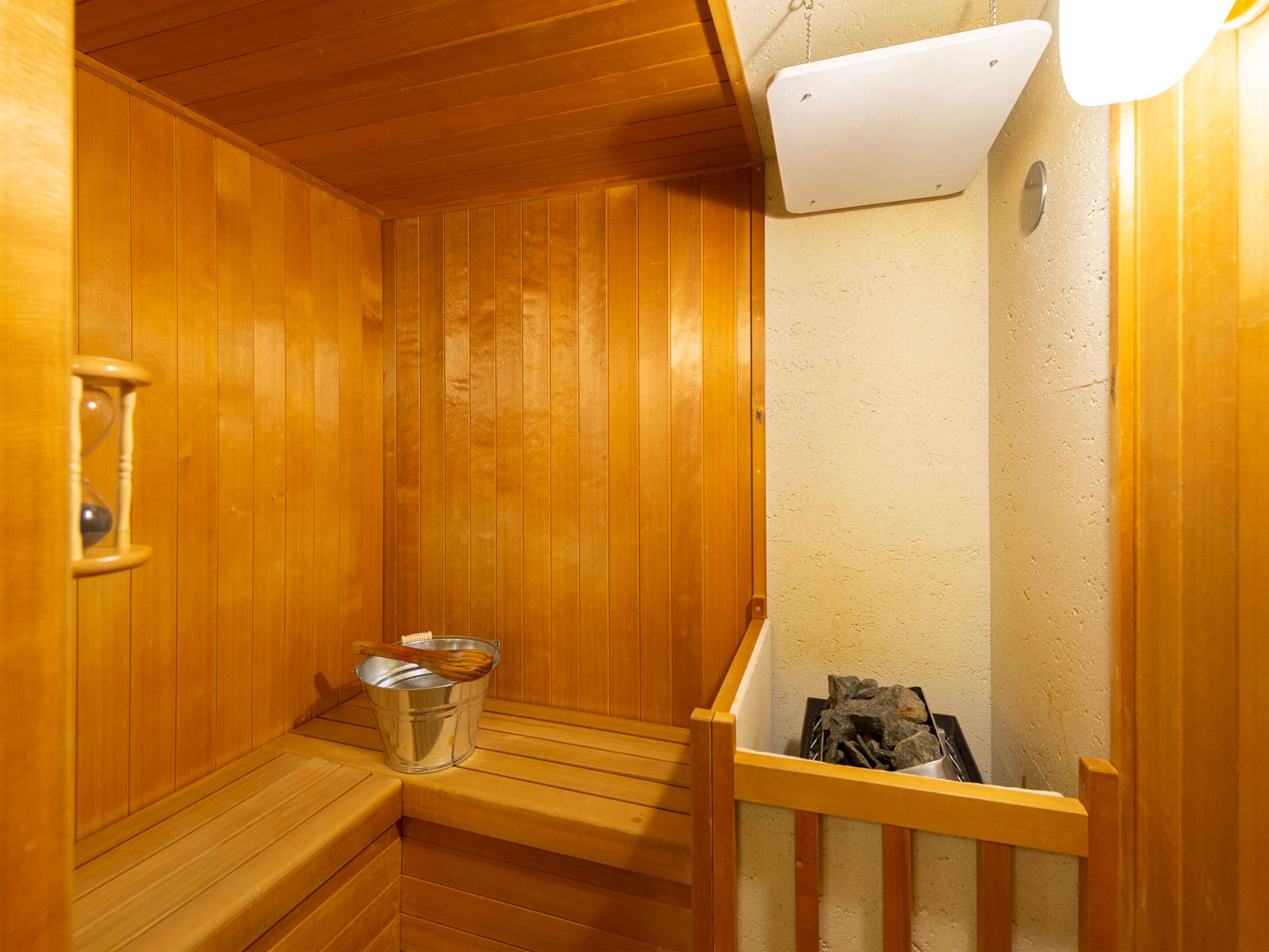 A wooden sauna with benches, a bucket, and a heater.