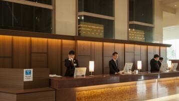 A hotel reception desk with a wooden finish, large windows, and a tiled floor.
