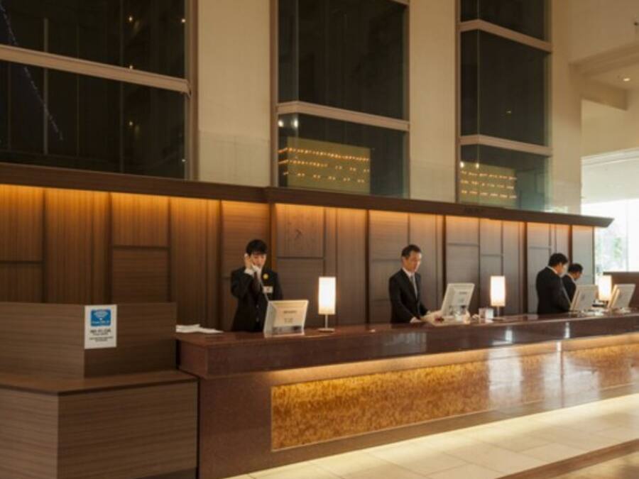 A hotel reception desk with a wooden finish, large windows, and a tiled floor.