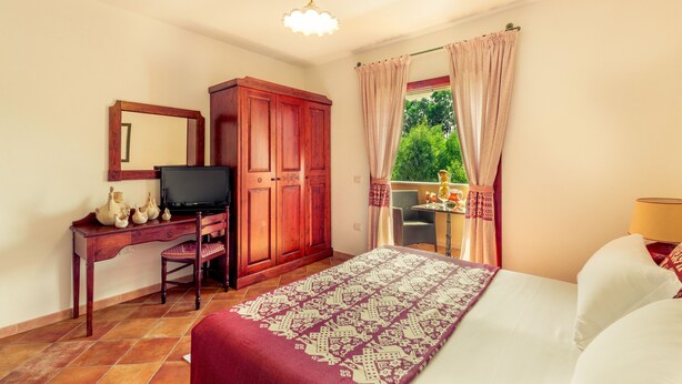 A bedroom with a bed, a desk with a television, a wardrobe, and a window with curtains. - Residence Sos Alinos (Orosei)