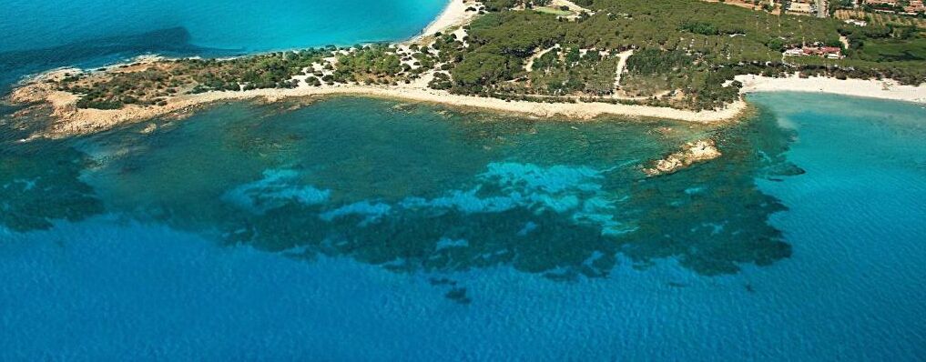 An aerial view of a coastal area with clear blue waters, a sandy beach, and a small island with vegetation.