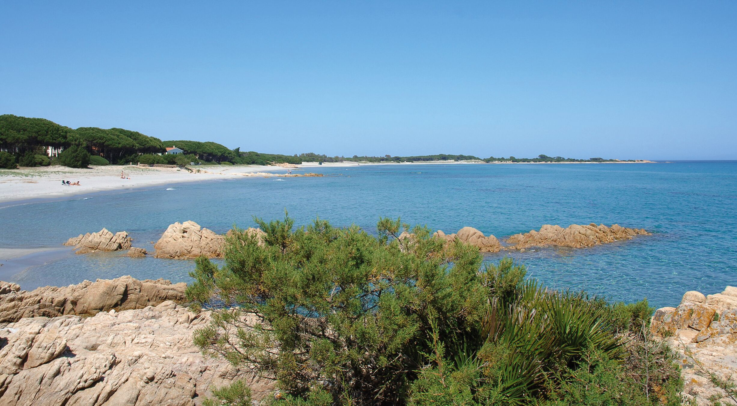 A coastal landscape with rocky outcrops, clear blue water, and a sandy beach.