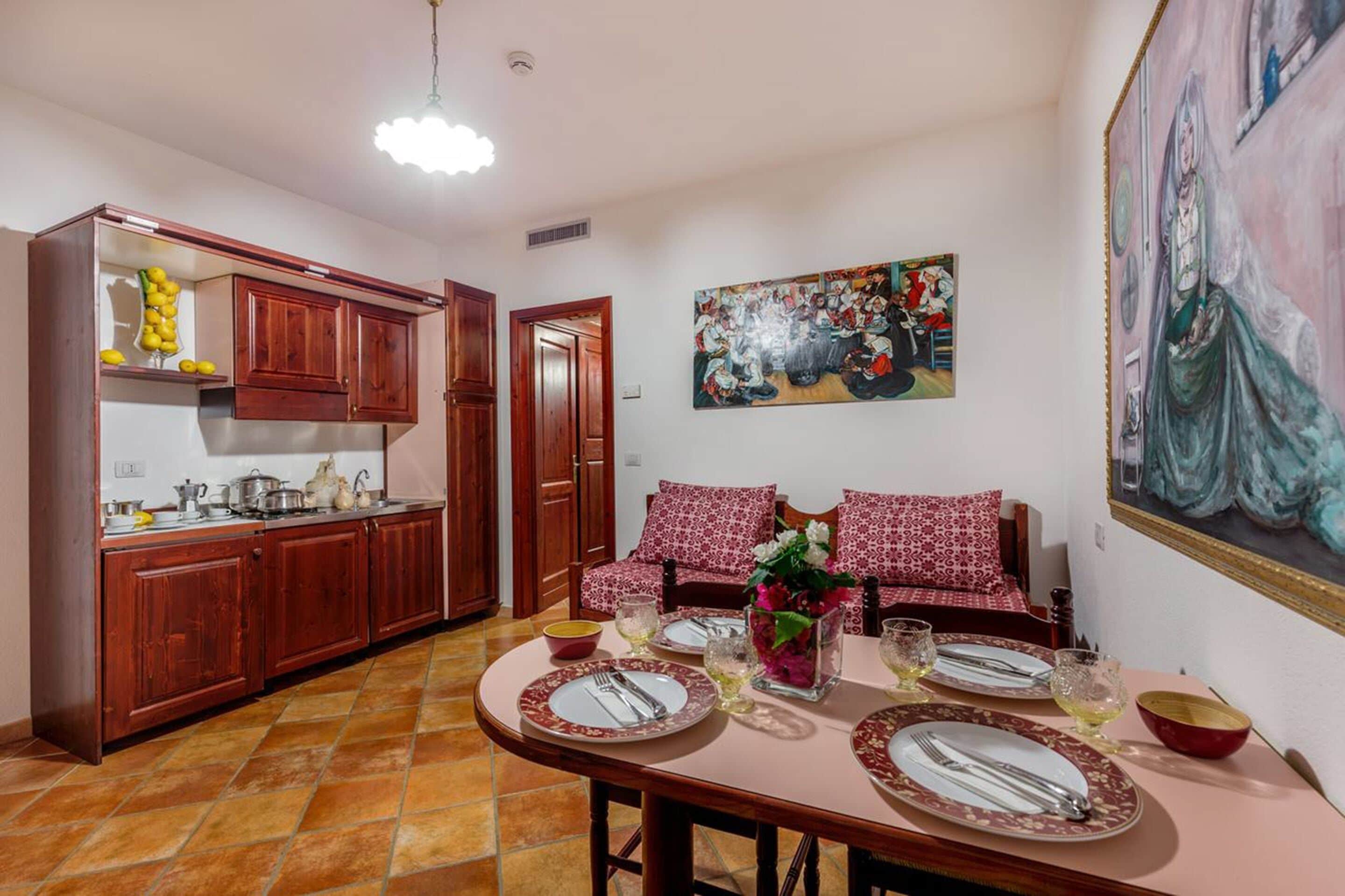 A dining area with a table set for four, a kitchen with wooden cabinets, and a painting on the wall.