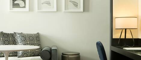 Una habitación moderna con un sofá, una pequeña mesa redonda, una silla, un cubo de basura y tres cuadros enmarcados en la pared.